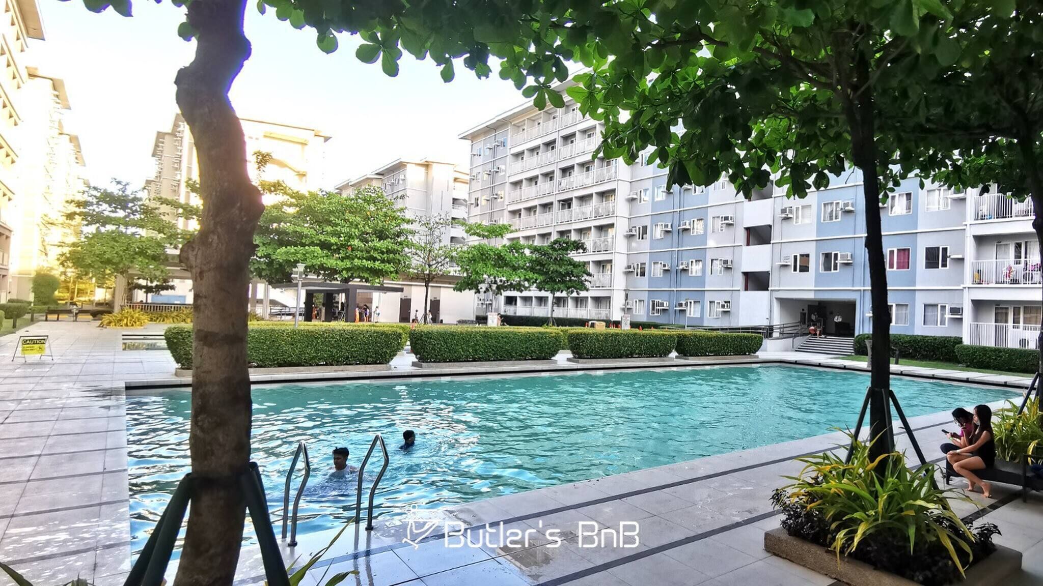 Una piscina rodeada de jardines, con un edificio de varios pisos al fondo.