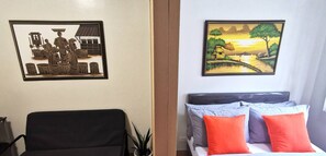 Une chambre d’hôtel avec un lit, une chaise, un tableau représentant un paysage de village accroché au mur et une plante en pot.