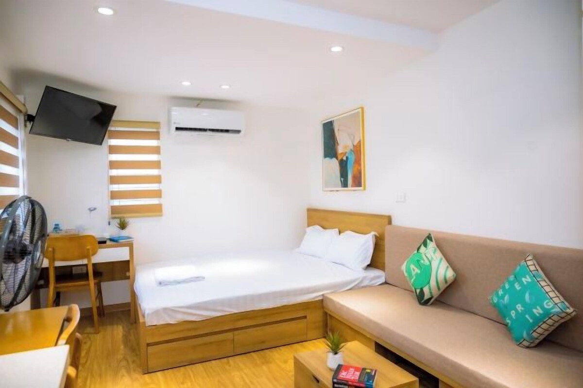 A compact hotel room with a bed, a sofa, a desk, and a TV.