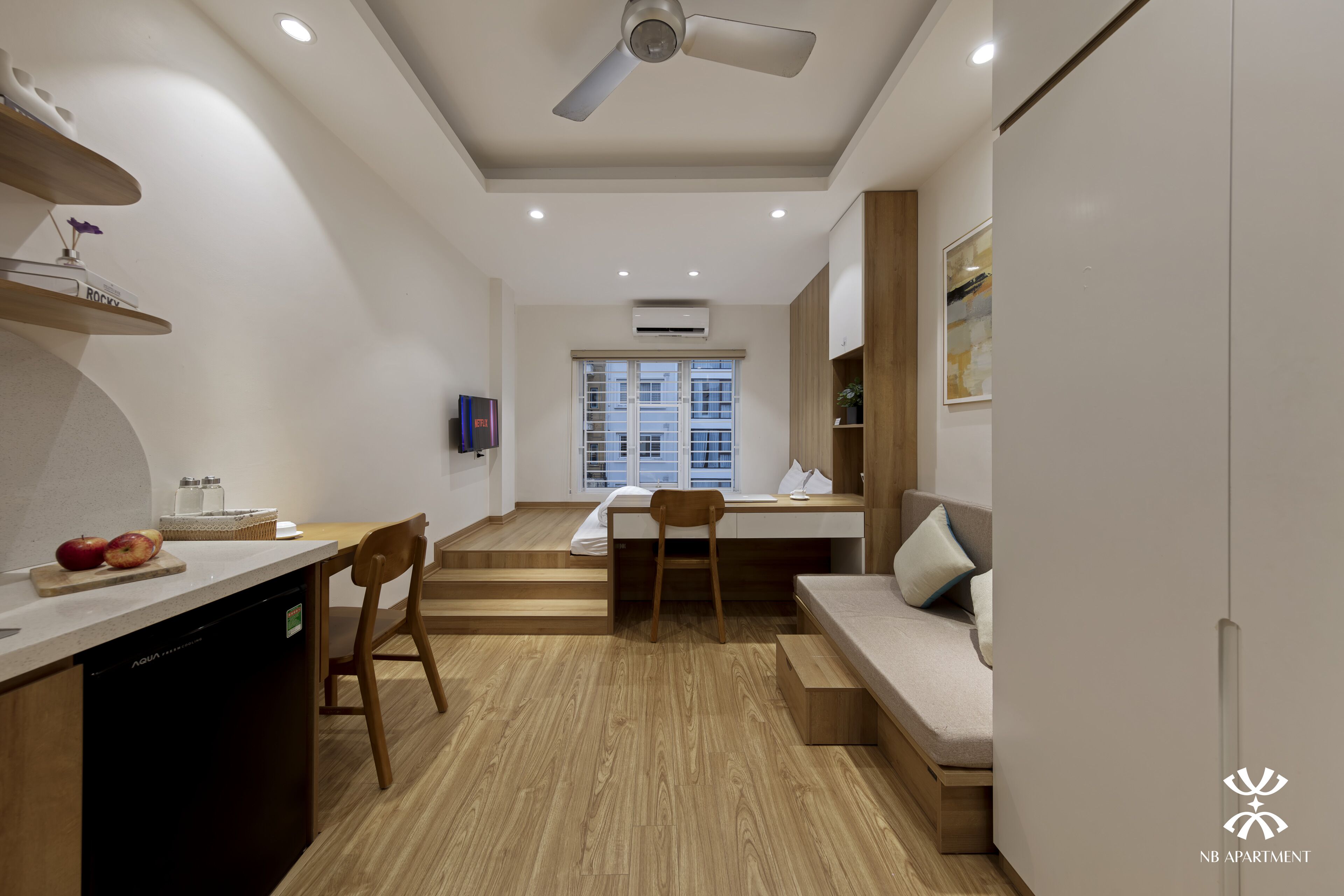 A modern apartment with a kitchen, dining area, and living space. It features a ceiling fan, recessed lighting, and a large window.