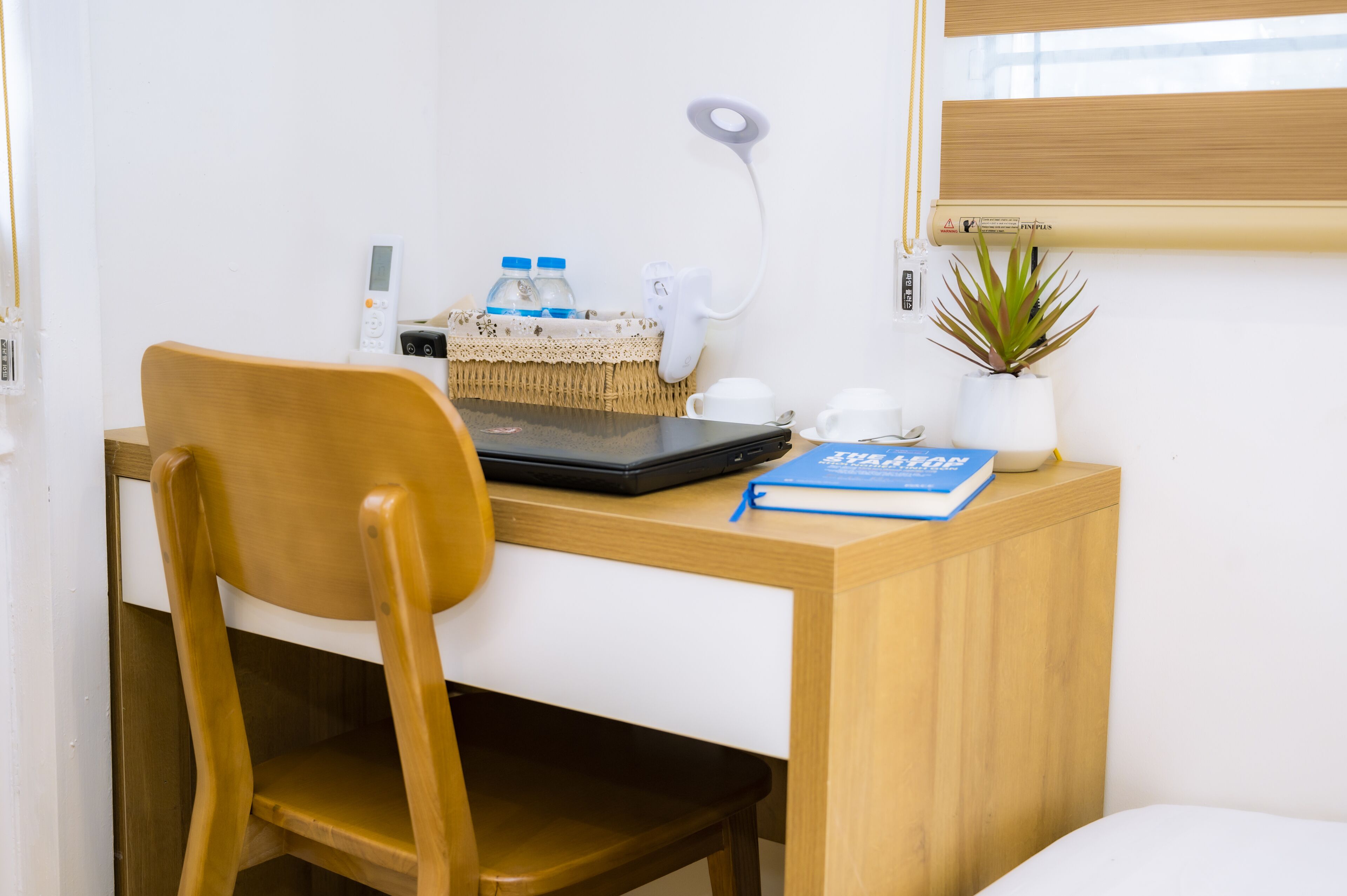 A wooden desk with a laptop, a small plant, a water bottle, and a cup.