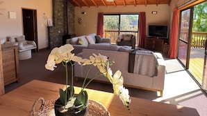 A spacious living area with a wooden ceiling, a sofa set, a television, and a large window with a view of the outdoors.