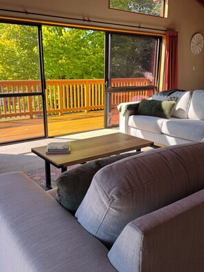 Un salon moderne avec un canapé, une table basse et une porte-fenêtre coulissante donnant sur une terrasse extérieure.
