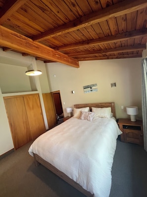 Une chambre avec un plafond en bois, un grand lit avec une literie blanche, deux tables de chevet avec des lampes et une armoire en bois.