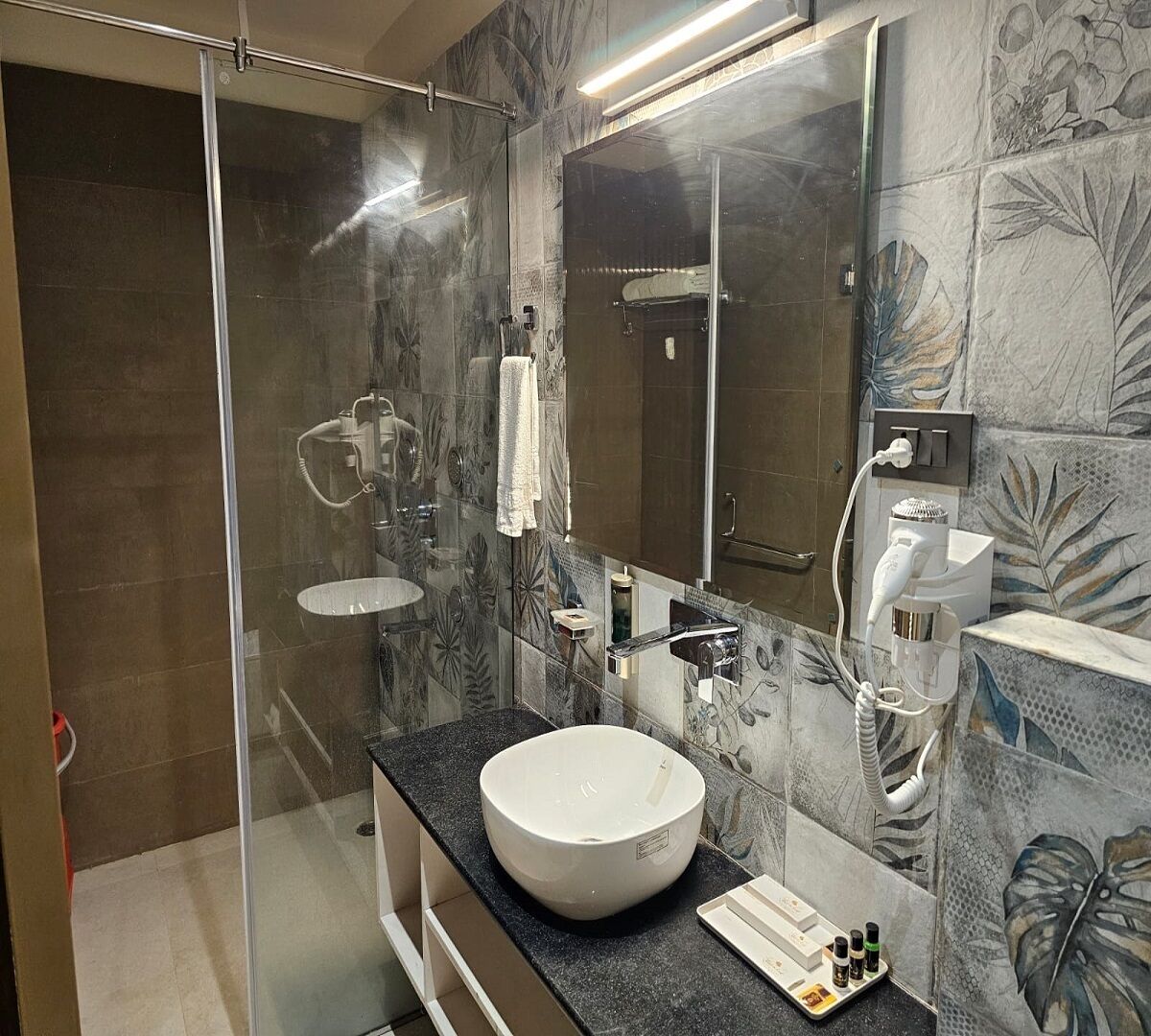 A modern bathroom with a glass-enclosed shower, a large round sink, and a mirror above the sink.
