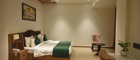 A modern hotel room with a wooden bed, a bedside table with a lamp, a chair, and a potted plant.