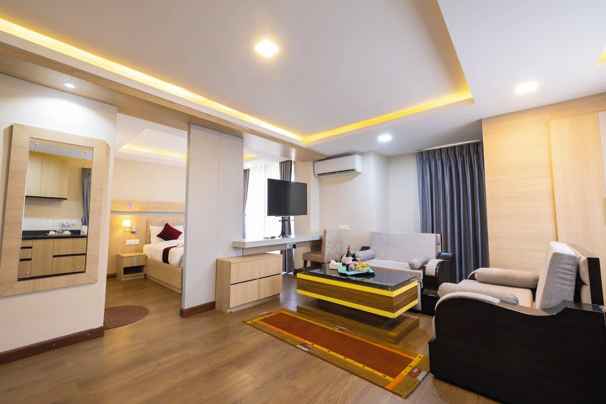 Quarto de hotel moderno com sofá, mesa de centro, televisão, escrivaninha e área de banheiro.