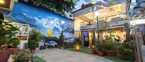 A restaurant with a mountain mural, potted plants, and a sign reading "Breakfast Lunch Dinner".