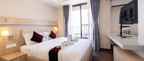 A modern hotel room with a large bed, bedside tables, a desk, and a TV mounted on the wall.