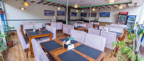 A restaurant with wooden tables, cushioned seating, and potted plants.