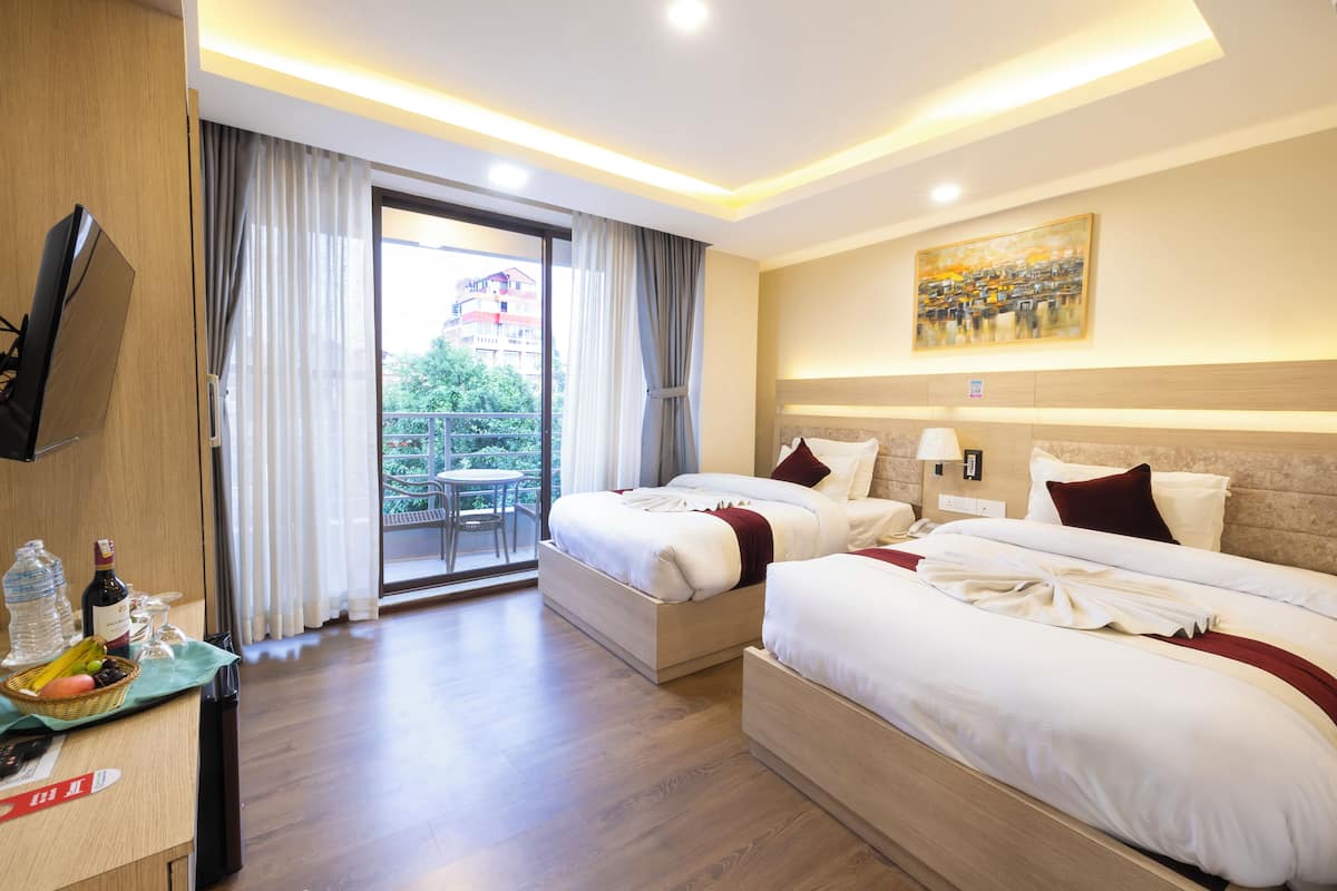Quarto de hotel com duas camas, televisão, mesa de jantar e varanda com vista para edifícios.