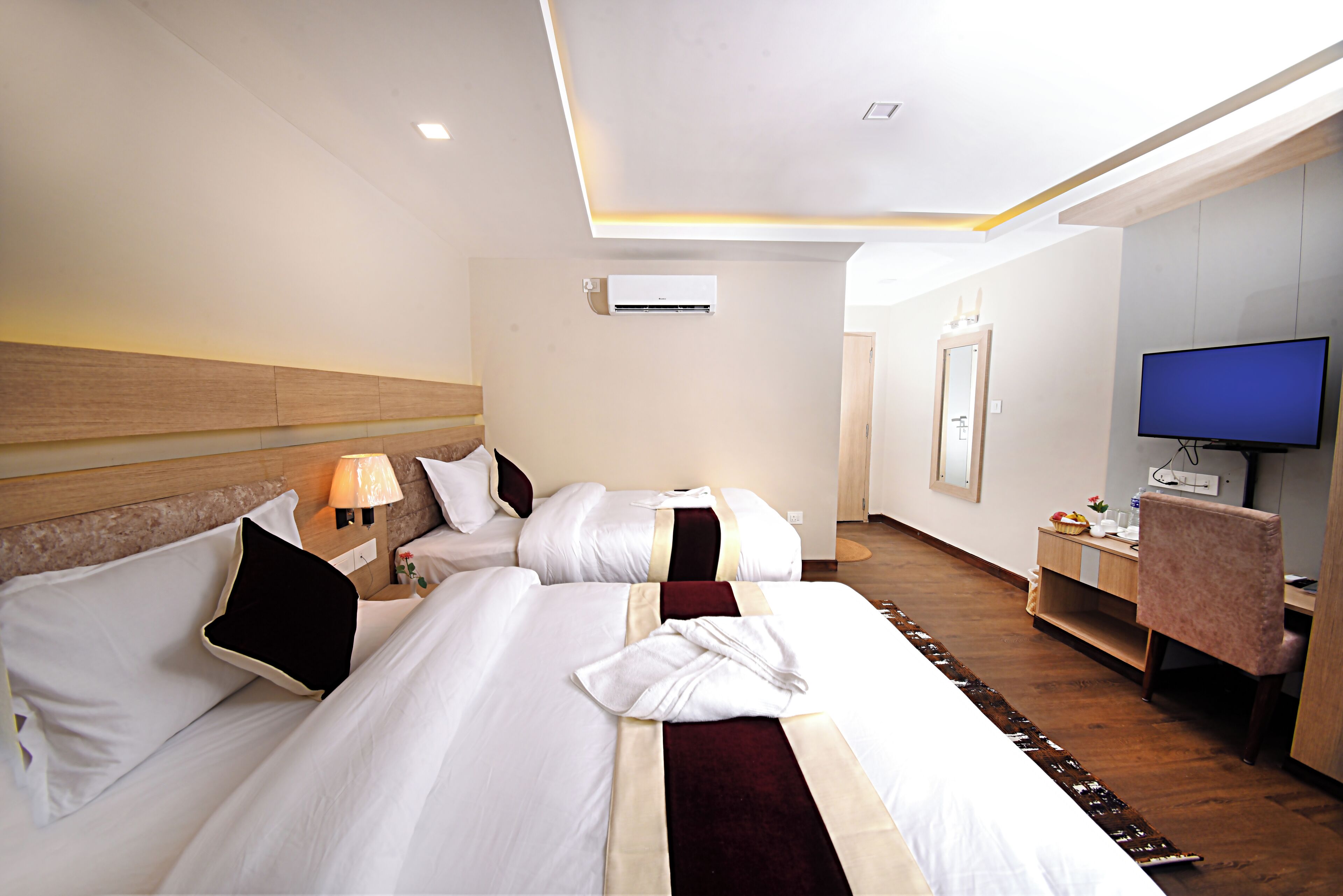 Habitación de hotel con dos camas, un escritorio, un televisor y aire acondicionado.