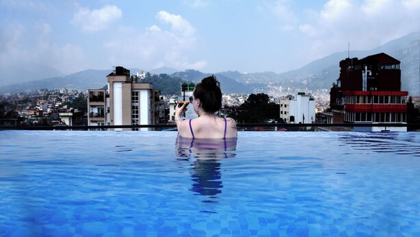A person in a swimming pool with a cityscape and mountains in the background. - Divine Kathmandu Hotel (Kathmandu)