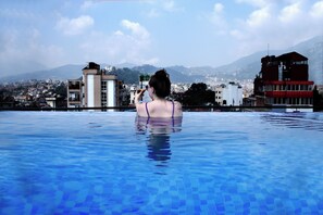 Una persona en una piscina con un paisaje urbano y montañas al fondo.