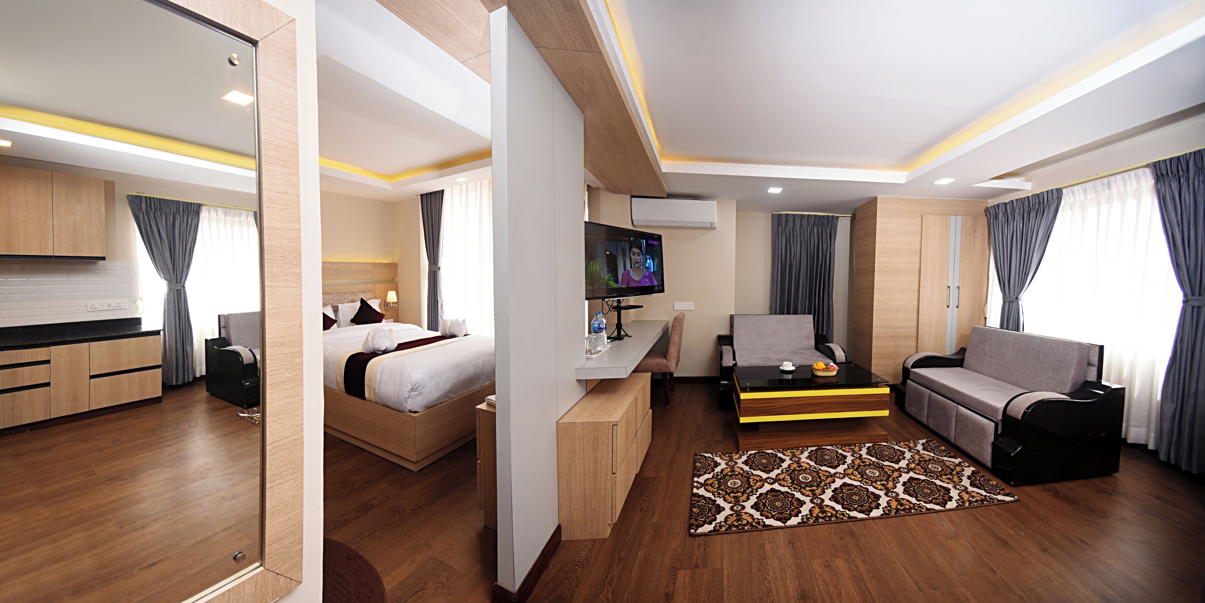 Una habitación de hotel moderna con cama, sofá, televisor, escritorio y zona de cocina.