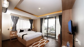 A modern hotel room with a large bed, a flat-screen TV, a balcony with a city view, and a wooden floor. - Divine Kathmandu Hotel (Kathmandu)