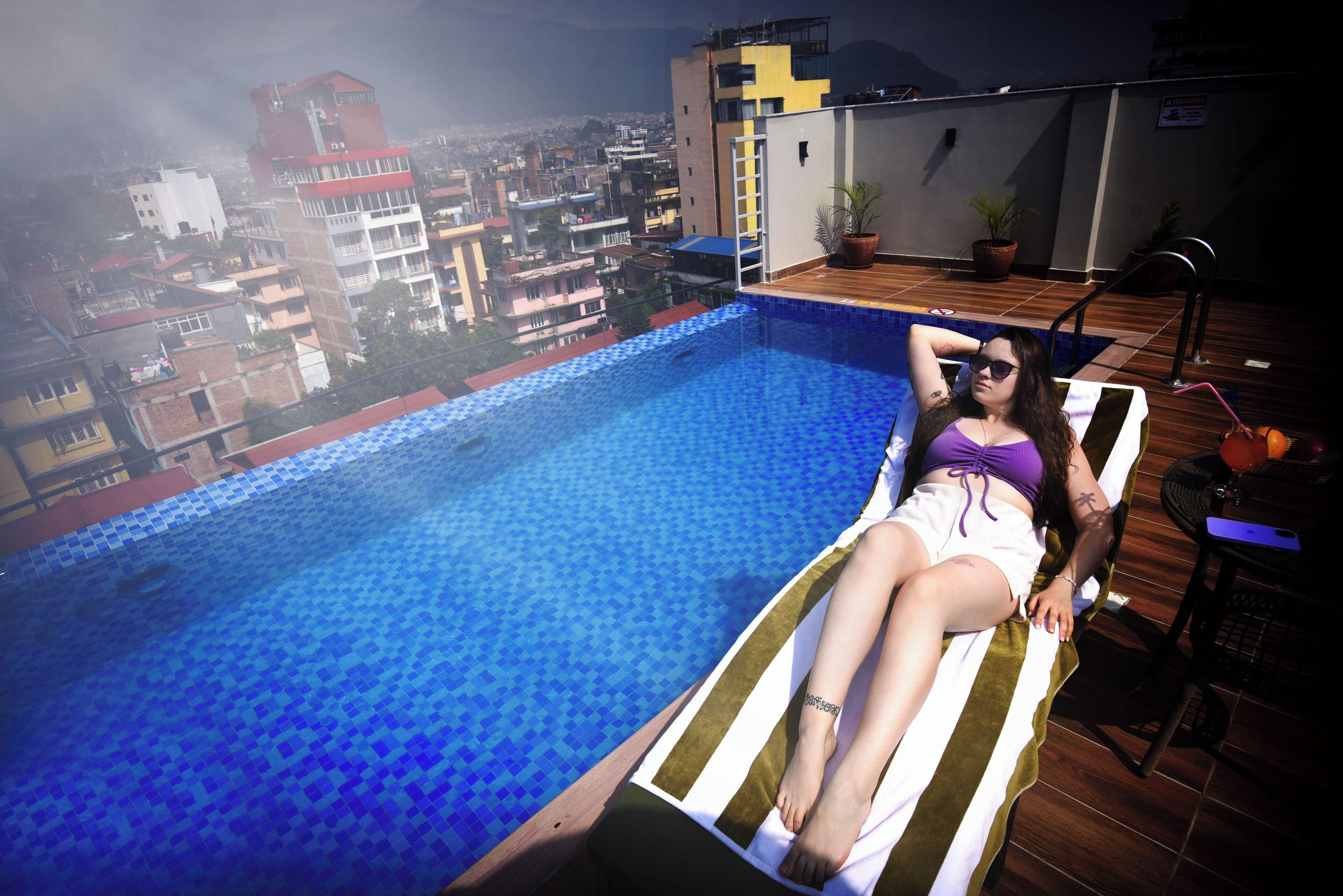 Une personne se détend au bord d’une piscine avec vue sur la ville.