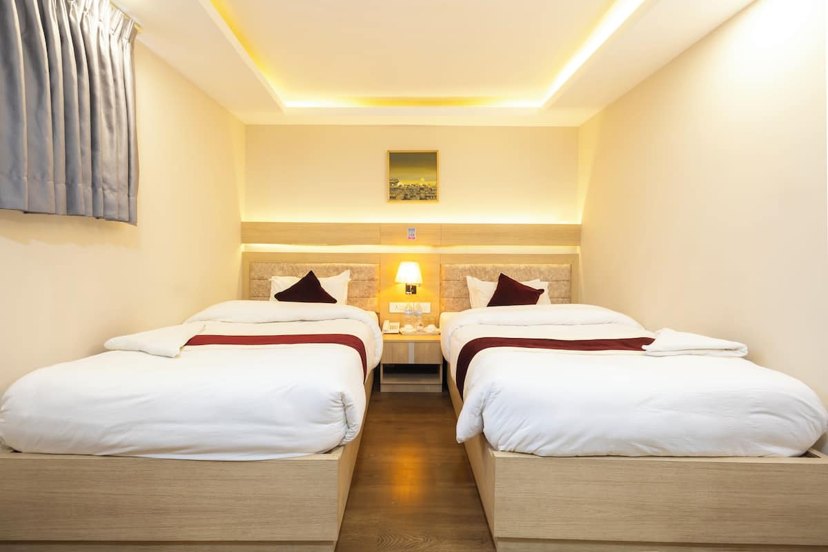 Quarto de hotel com duas camas de solteiro, mesa de cabeceira com abajur, um quadro na parede e piso de madeira.