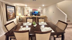 Un comedor con una mesa grande dispuesta para seis personas, un televisor al fondo y una escalera a la derecha.