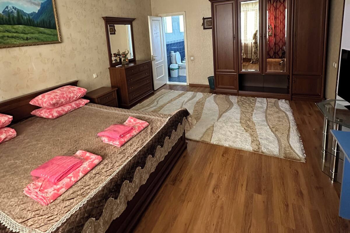 A bedroom with a large bed, wooden wardrobe, and a mirror.