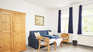 A room with a blue sofa, wicker chairs, a wooden wardrobe, and a window with curtains.