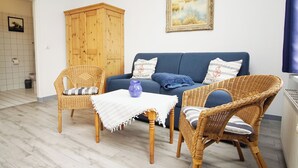 A living room with a blue sofa, wicker chairs, a small table with a vase, and a wooden cabinet.