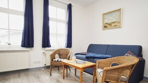 A room with a blue sofa, wicker chairs, a wooden table, and a window with curtains. - Die Ferienwohnung Nr. 02 im Haus Rugier in Göhren (Göhren)