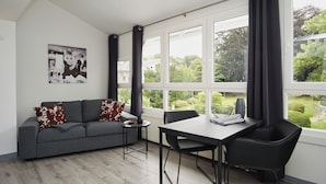 A modern living room with a grey sofa, black chairs, a small table, and a large window with curtains. - Die Ferienwohnung Nr. 04 im Haus Rugier in Göhren (Göhren)
