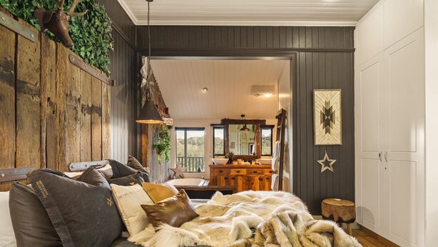 Ein gemütliches Schlafzimmer mit einem großen Bett, einem Holzkopfteil, einem Schminktisch und Blick ins Freie.