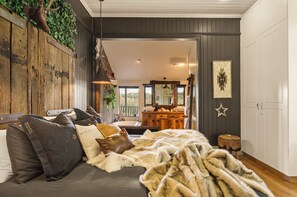 A cozy bedroom with a large bed, a wooden headboard, a dresser, and a view of the outdoors.