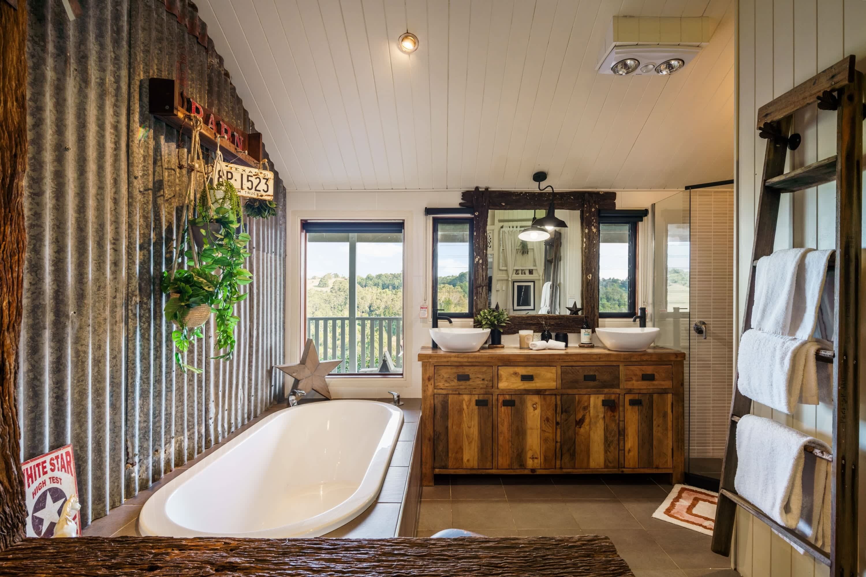 Ein Badezimmer mit einer großen Badewanne, einem Holzwaschtisch und Blick ins Freie.