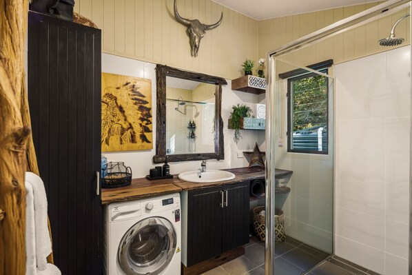 A modern bathroom with a washing machine, a sink, a mirror, and a shower.