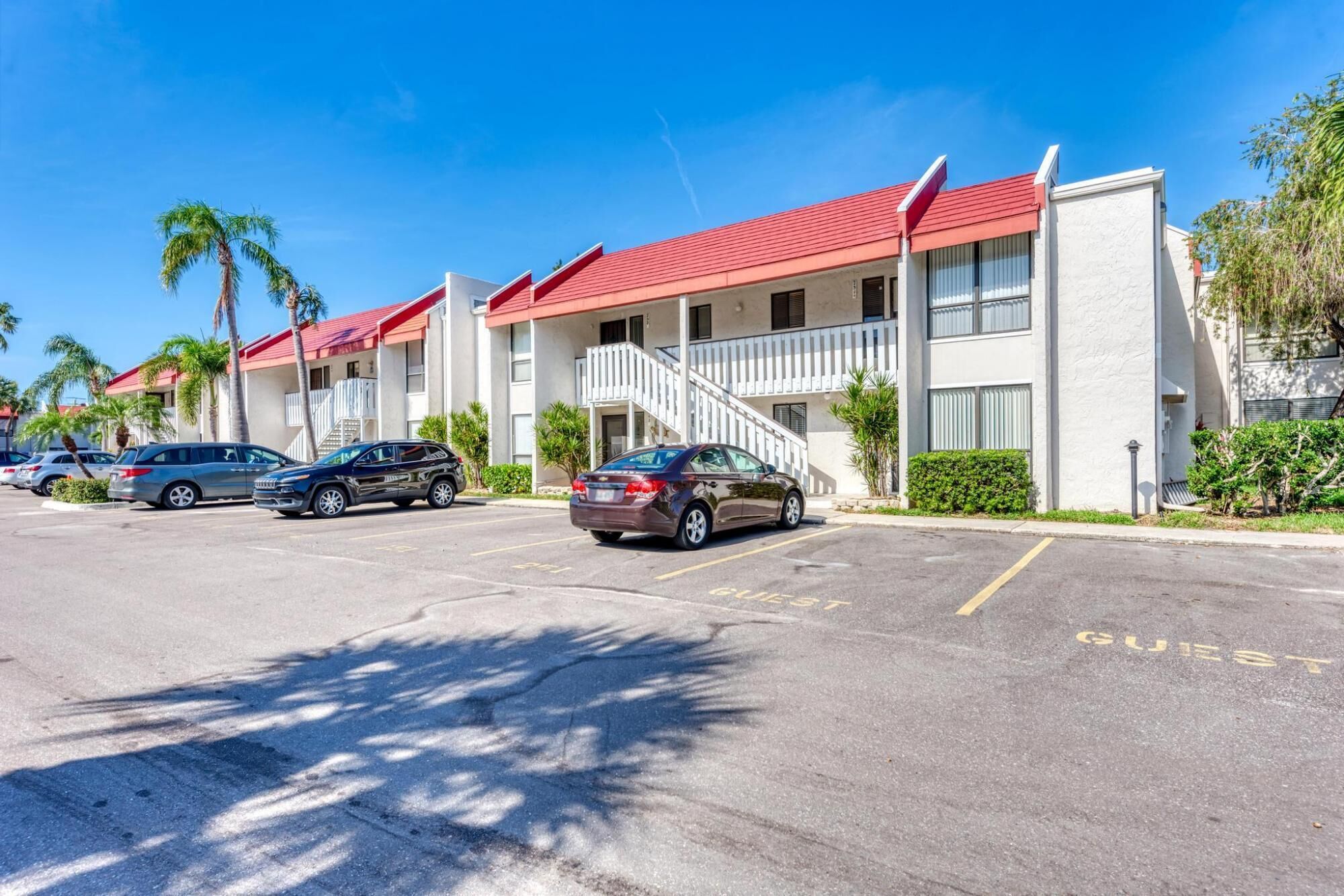 A row of motel buildings with a red roof, a parking lot, and a few cars parked in front.