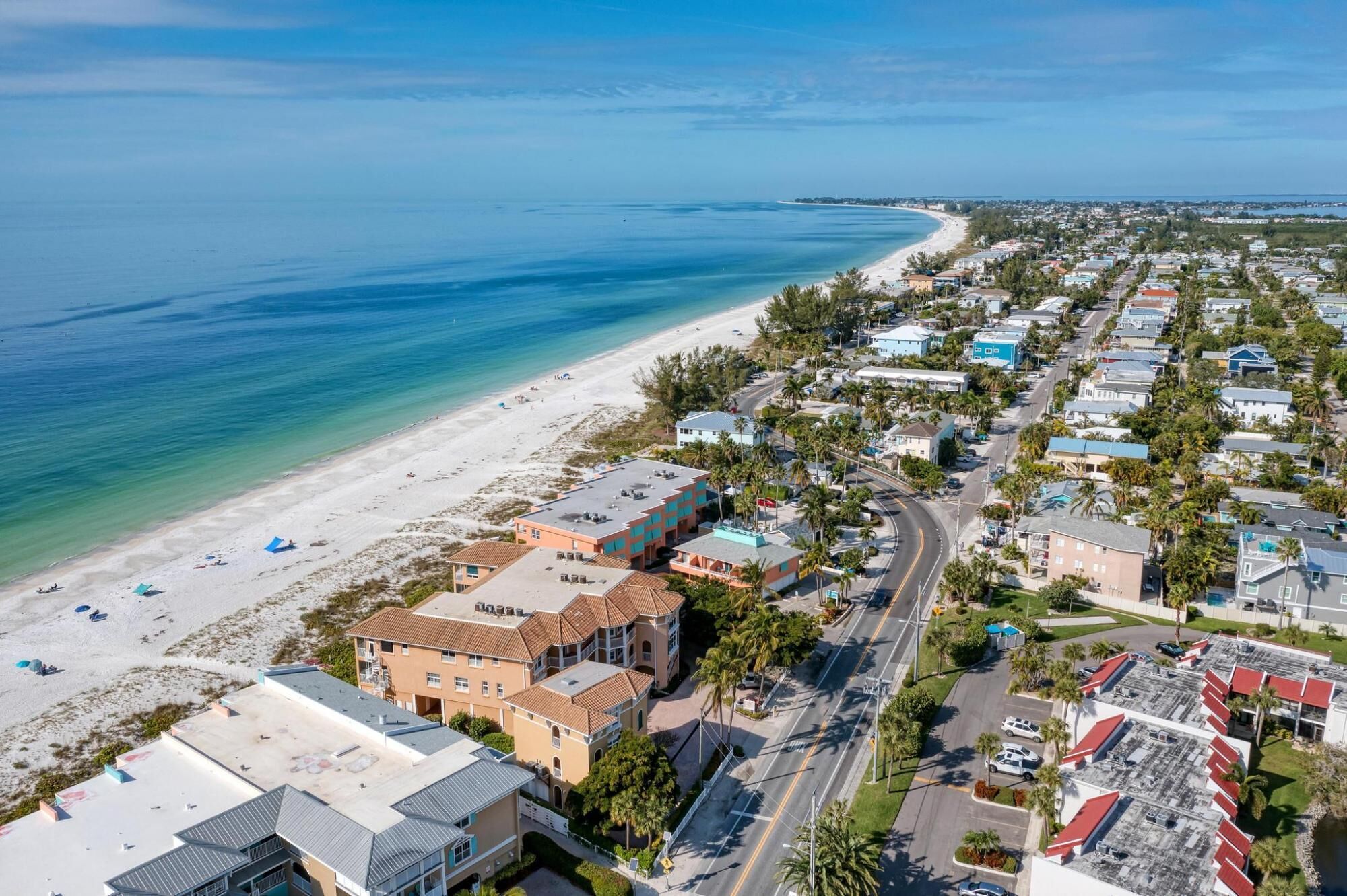 An aerial view of a coastal town with a beach, residential buildings, and a road.