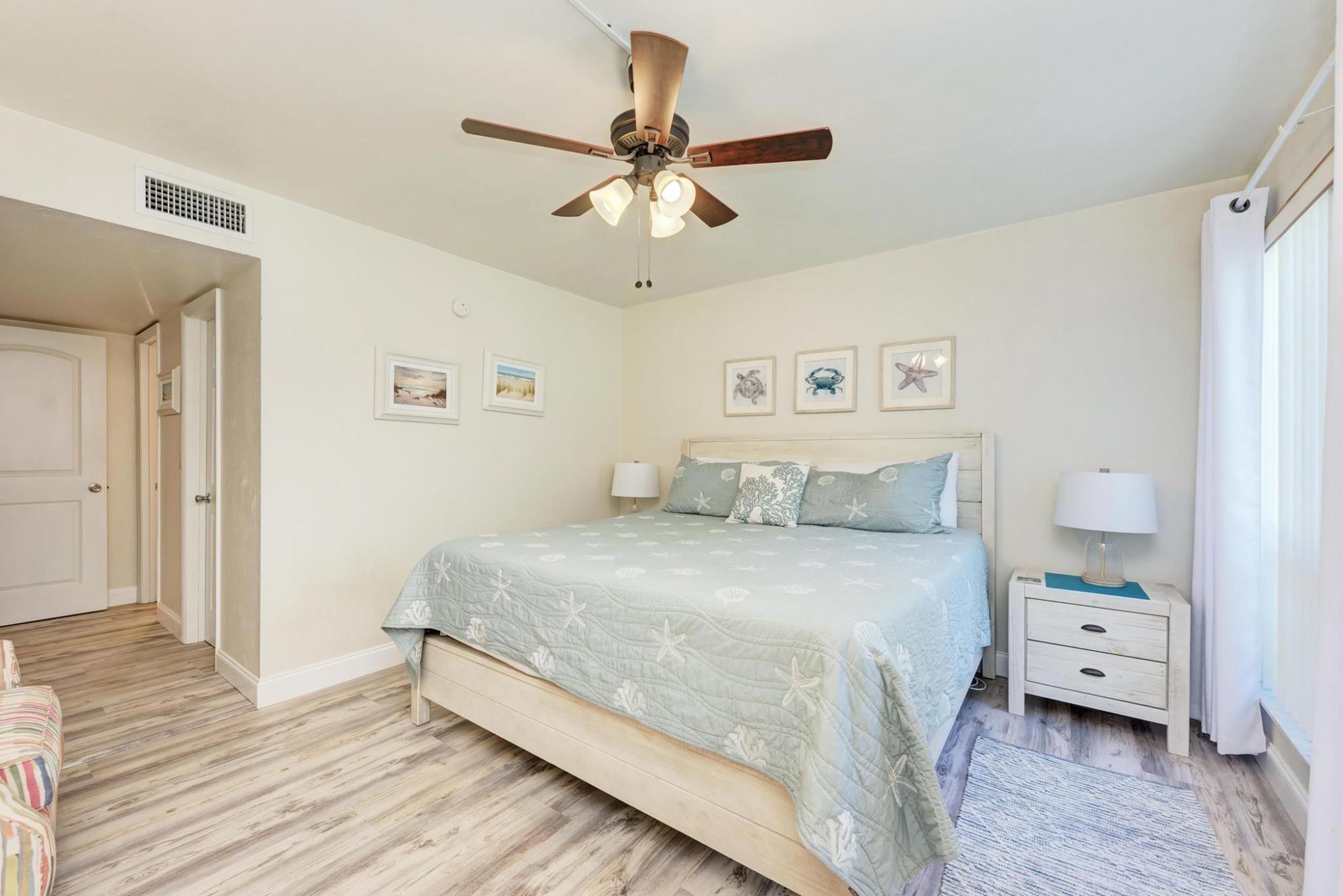 A bedroom with a bed, nightstands, a ceiling fan, and framed pictures on the wall.