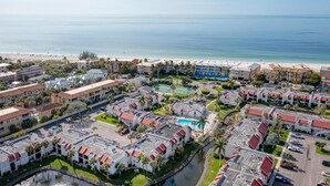Luftaufnahme eines Küstenresorts mit mehreren Gebäuden, einem Swimmingpool und einem Strand im Hintergrund.