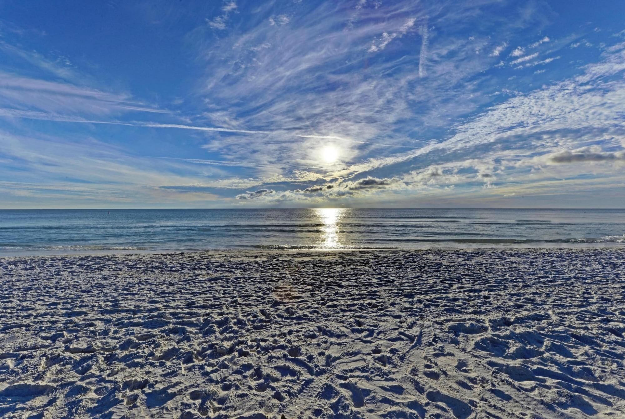 A beach with visible footprints and a clear sky with clouds.