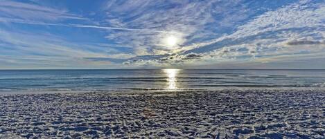 A beach with visible footprints and a clear sky with clouds.