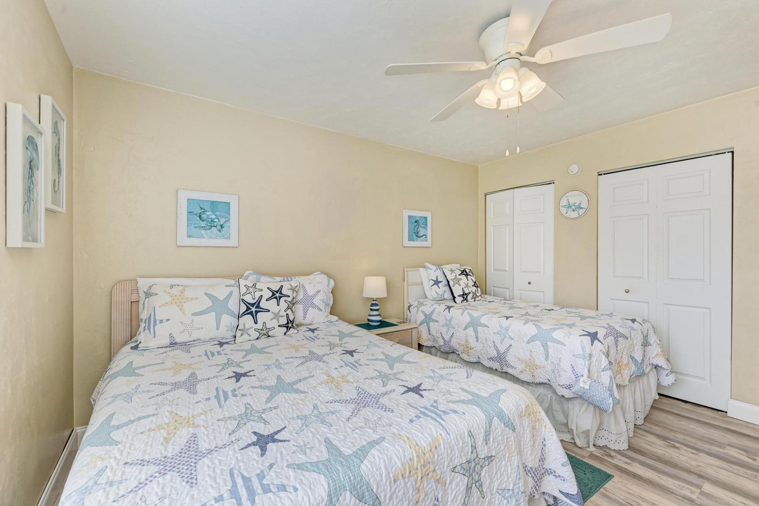 A bedroom with two beds, each with star-patterned bedding, a ceiling fan, and artwork on the walls.