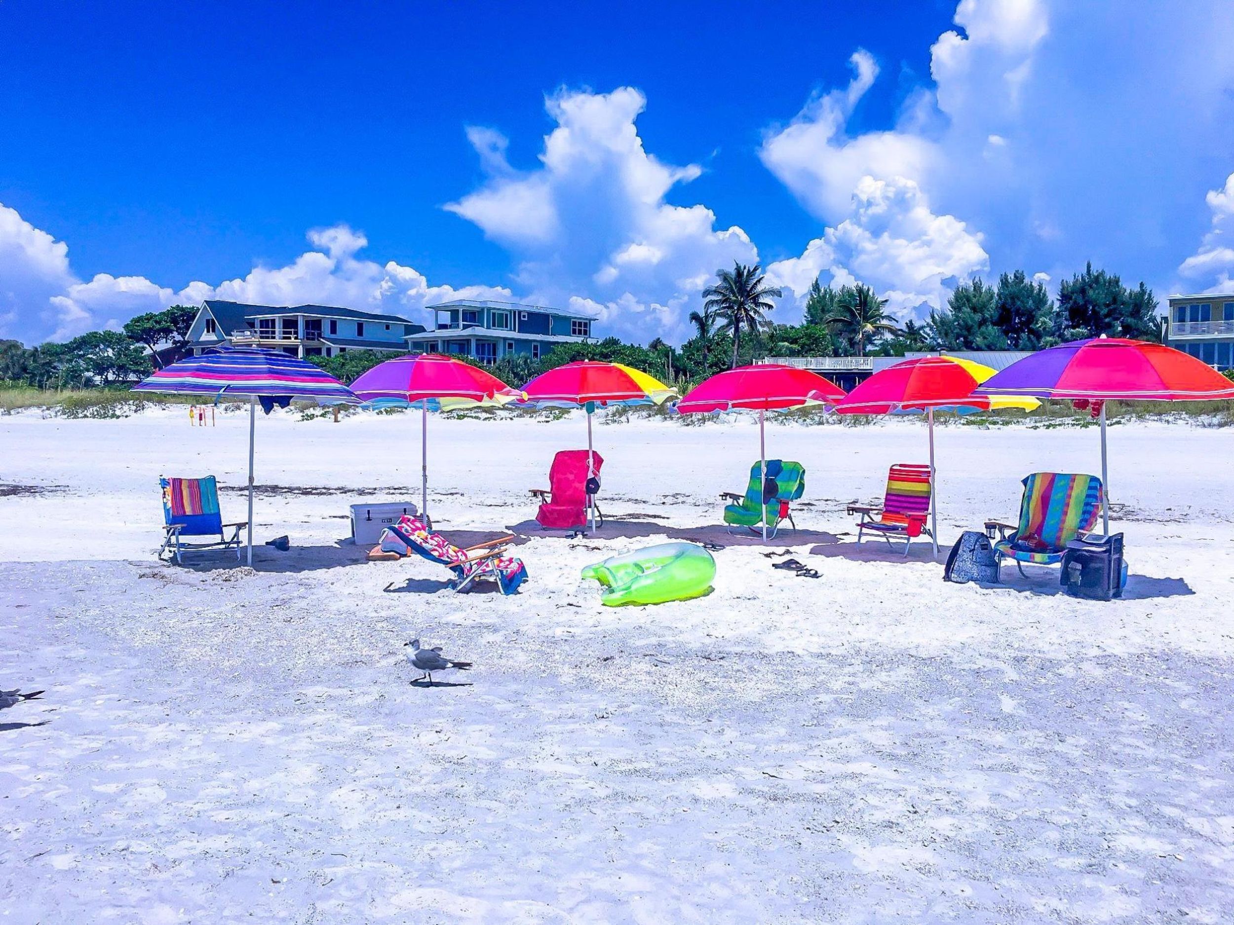 A beach with colorful umbrellas and beach chairs, a seashore, and a building in the background.