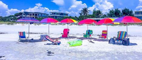 A beach with colorful umbrellas and beach chairs, a seashore, and a building in the background.