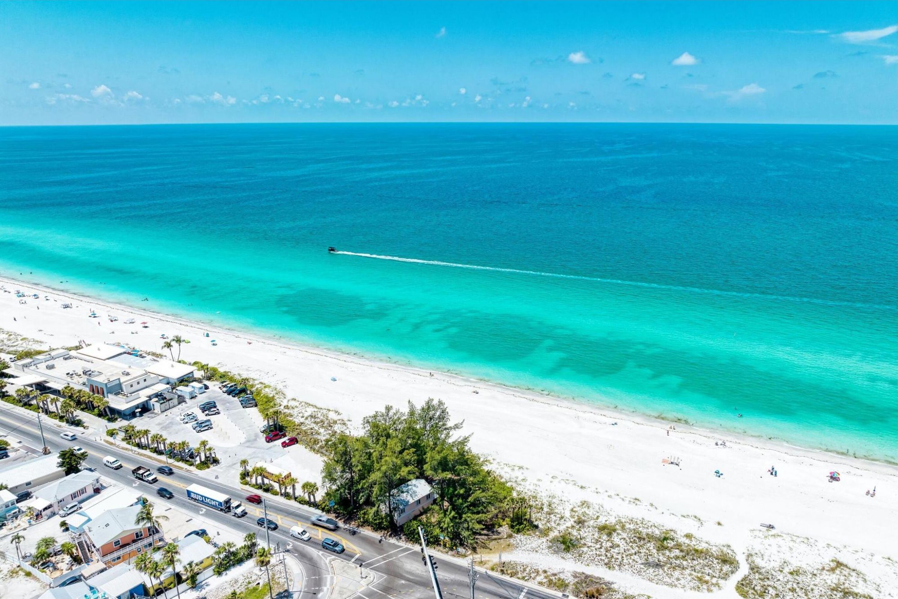 An aerial view of a coastal area with a beach, a road, and buildings.