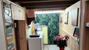 A narrow hallway leading to a kitchen with a refrigerator and a sink. There are signs on the walls and a potted plant on the table. - Studio Meublé Indépendant Dans un Ancien Moulin (Ceton)