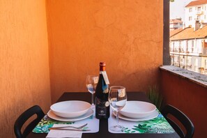Una mesa de comedor dispuesta con platos, cubiertos y una botella de vino en un balcón con vistas a edificios.