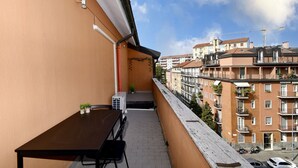 Een smal balkon met een tafel en stoelen, uitkijkend op een woongebied met meerdere gebouwen en een hijskraan op de achtergrond.