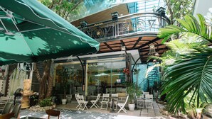 An outdoor cafe with tables and chairs, potted plants, and a green umbrella. - Nguyen Huong Hotel (Da Nang)
