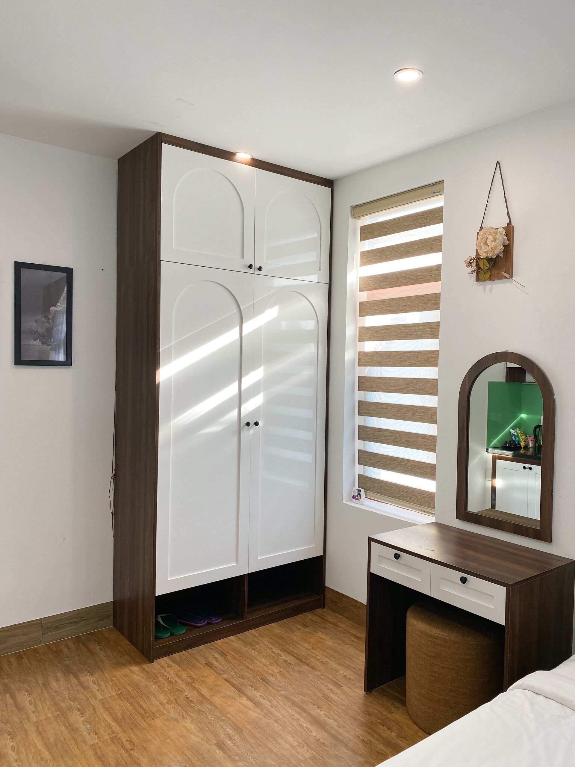 A bedroom with a wardrobe, a vanity with a mirror, and a window with blinds.