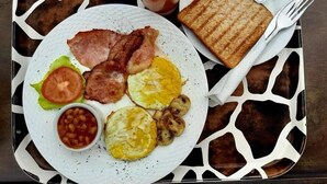 Ein Frühstücksbrett mit Toast, Speck, Eiern, Tomaten, Bohnen und einem Glas Saft.
