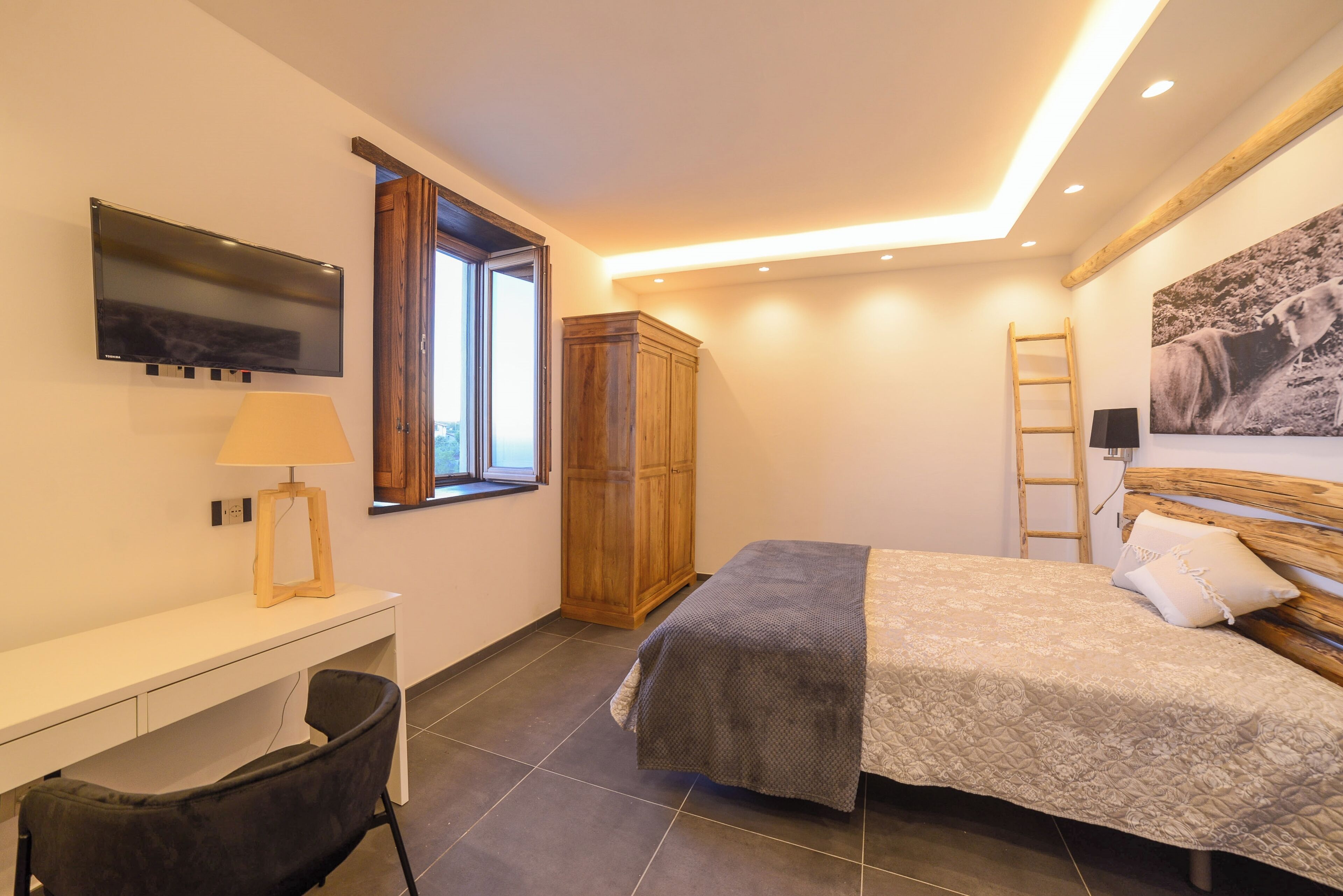 Une chambre à coucher comprenant un lit, un bureau, une chaise, une armoire, un téléviseur, une fenêtre et un tableau accroché au mur.