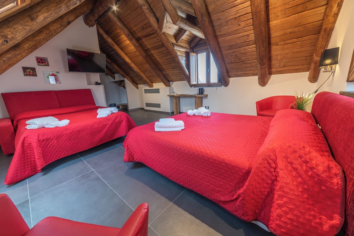 Habitación de hotel con dos camas rojas, un televisor y techo de madera.